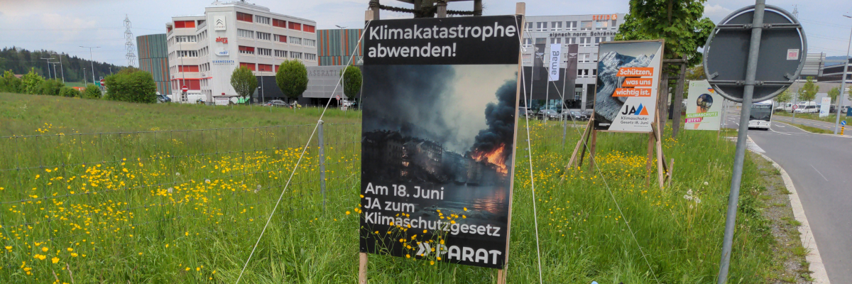 Im Vordergrund ein Plakat der PARAT mit dem Titel "Klimakatastrophe abwenden!". Im Hintergrund weitere Plakate anderer Parteien.